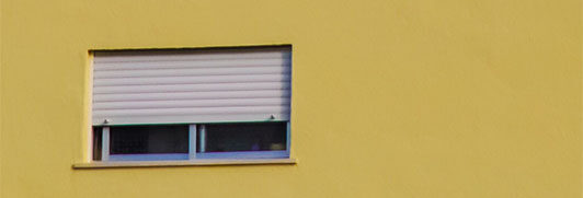 Eine Hauswand mit einem Fenster, dass den Rollladen zu Hälfte unten hat.